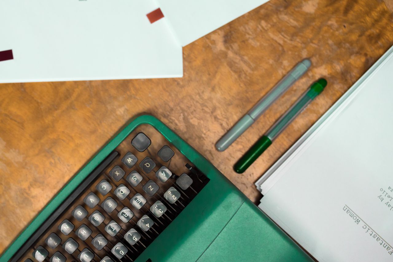 About Flat lay of a green vintage typewriter, papers, and pens on a wooden desk.